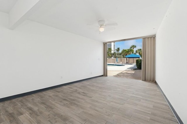 spare room featuring expansive windows, ceiling fan, and light hardwood / wood-style flooring