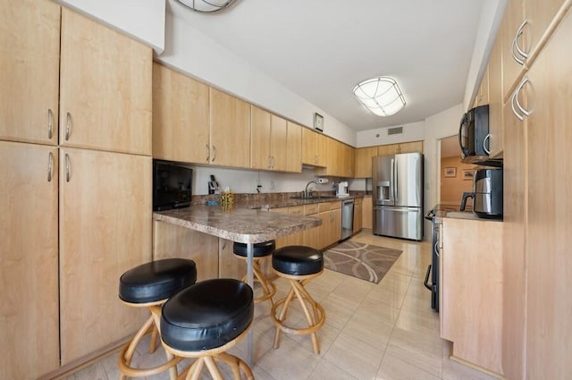 kitchen with light brown cabinetry, sink, stainless steel appliances, and kitchen peninsula