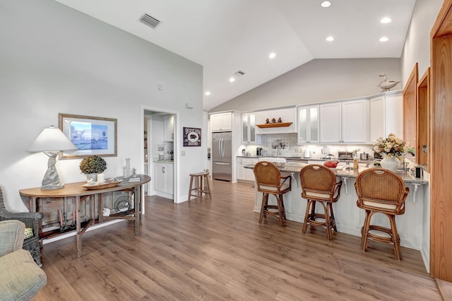 kitchen with hardwood / wood-style floors, white cabinetry, stainless steel fridge, a kitchen bar, and kitchen peninsula