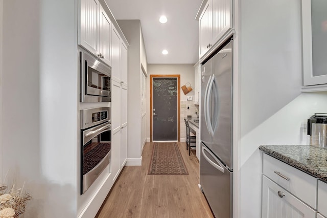 kitchen with stone counters, white cabinetry, backsplash, stainless steel appliances, and light wood-type flooring