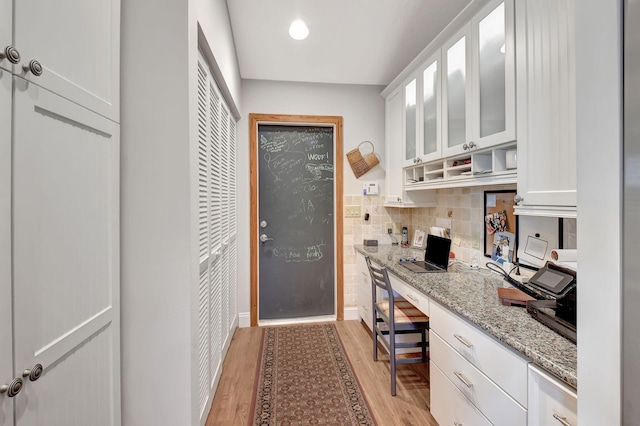 kitchen featuring built in desk, backsplash, white cabinets, light stone counters, and light wood-type flooring