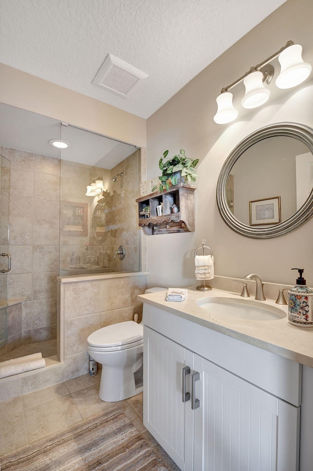 bathroom with tile patterned flooring, a tile shower, vanity, a textured ceiling, and toilet