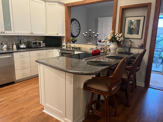 kitchen featuring stainless steel dishwasher, dark stone counters, kitchen peninsula, and a breakfast bar area