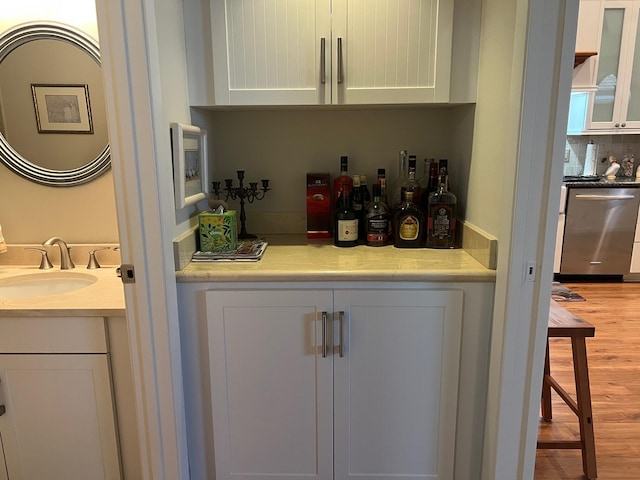 bar featuring sink, tasteful backsplash, stainless steel dishwasher, hardwood / wood-style flooring, and white cabinets