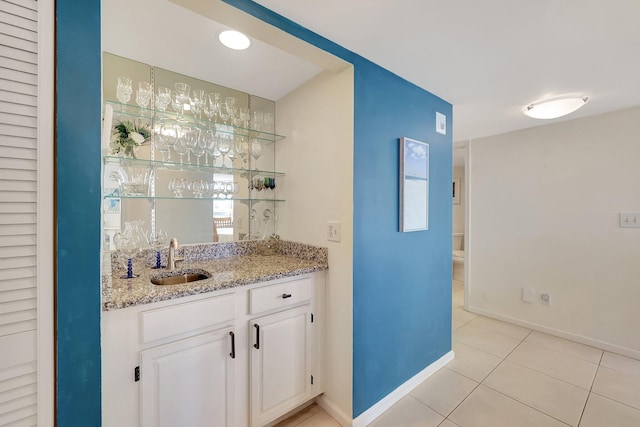 bar with light stone counters, light tile patterned floors, sink, and white cabinets