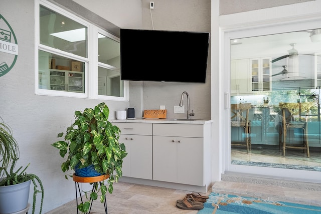 bar with white cabinetry, sink, and ceiling fan