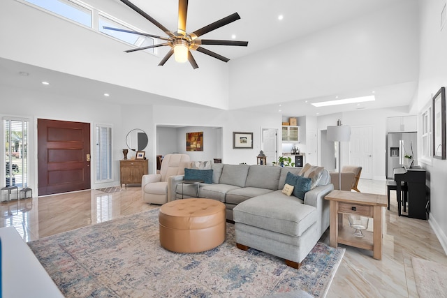 living room with ceiling fan, a towering ceiling, and a skylight