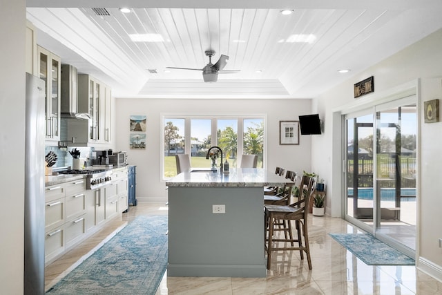 kitchen featuring a breakfast bar, a wealth of natural light, stainless steel gas stovetop, wooden ceiling, and wall chimney exhaust hood