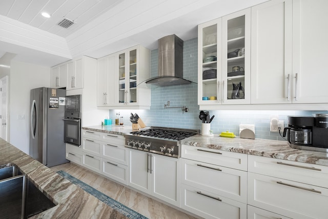 kitchen with appliances with stainless steel finishes, white cabinets, decorative backsplash, light stone countertops, and wall chimney exhaust hood