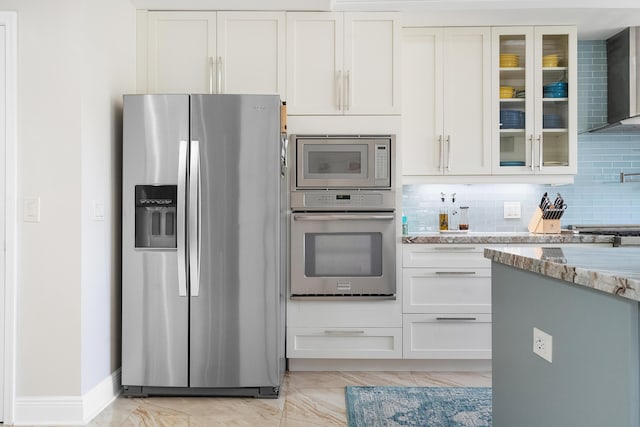 kitchen with tasteful backsplash, appliances with stainless steel finishes, white cabinets, light stone countertops, and wall chimney range hood