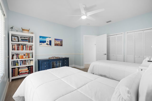 bedroom with dark wood-type flooring, ceiling fan, and two closets