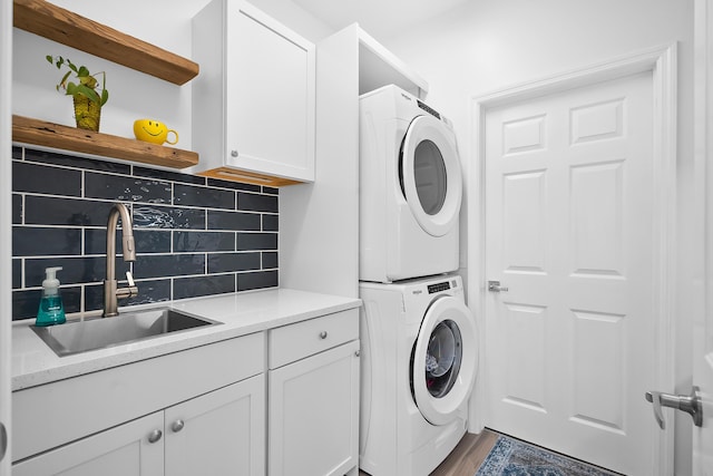 laundry area featuring cabinets, stacked washer and clothes dryer, sink, and wood-type flooring