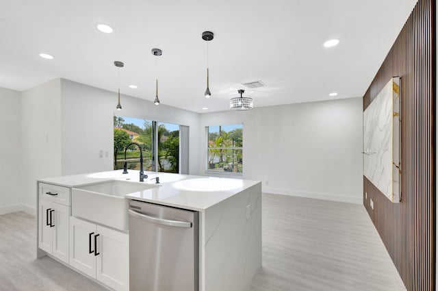 kitchen with wood walls, white cabinets, stainless steel dishwasher, light stone countertops, and a center island with sink