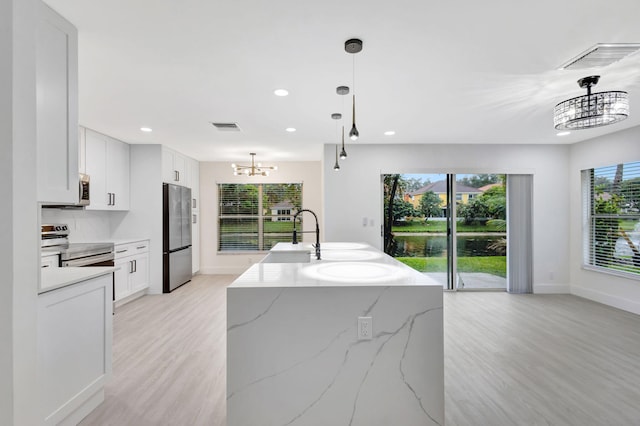 kitchen featuring white cabinetry, stainless steel appliances, light stone countertops, and hanging light fixtures