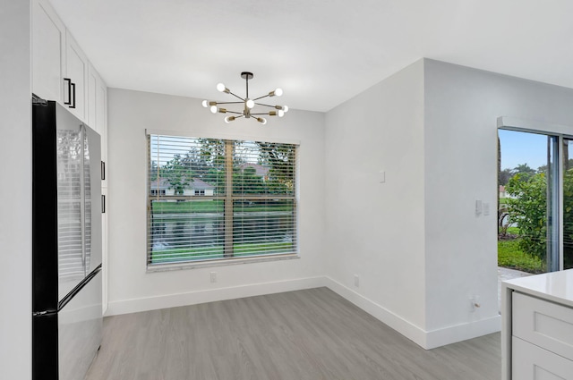 unfurnished dining area featuring light wood-type flooring and an inviting chandelier