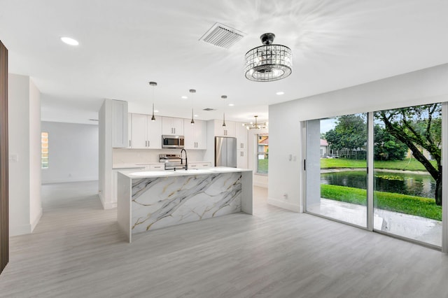 kitchen with white cabinetry, hanging light fixtures, a center island with sink, a notable chandelier, and stainless steel appliances