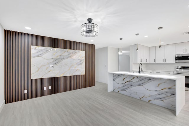 kitchen with sink, white cabinetry, hanging light fixtures, stainless steel appliances, and light hardwood / wood-style floors