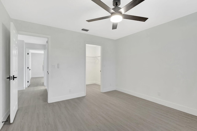 unfurnished bedroom with light wood-type flooring, a spacious closet, ceiling fan, and a closet