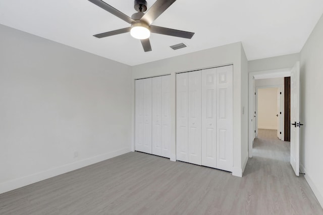 unfurnished bedroom featuring multiple closets, light wood-type flooring, and ceiling fan