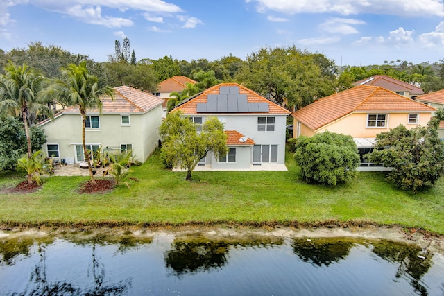 back of house with a water view, a lawn, and solar panels