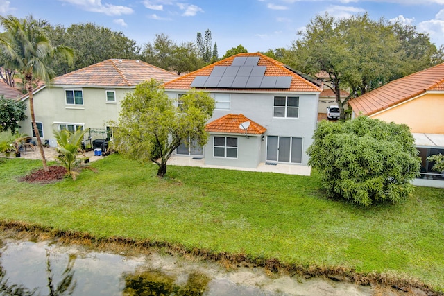 back of property featuring a water view, a yard, and solar panels