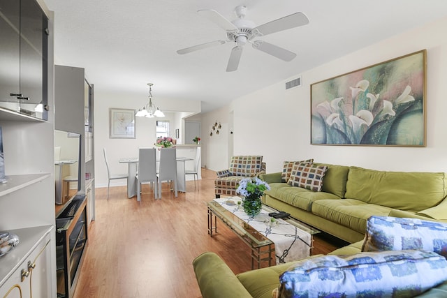 living room with ceiling fan with notable chandelier and light hardwood / wood-style flooring