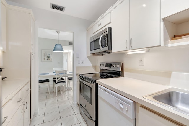 kitchen with pendant lighting, sink, white cabinets, light tile patterned floors, and stainless steel appliances