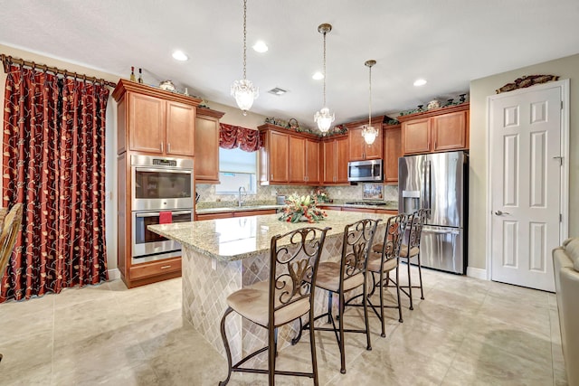 kitchen featuring a kitchen bar, light stone counters, a center island, hanging light fixtures, and appliances with stainless steel finishes