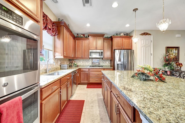 kitchen featuring sink, light stone counters, appliances with stainless steel finishes, pendant lighting, and backsplash