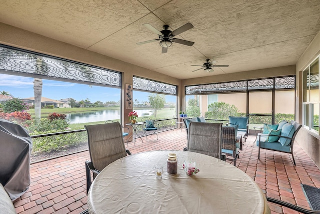 sunroom with ceiling fan and a water view