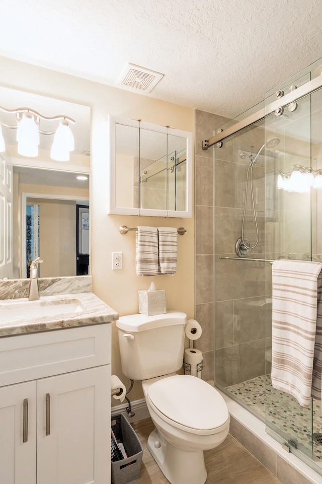 bathroom featuring vanity, toilet, an enclosed shower, and a textured ceiling