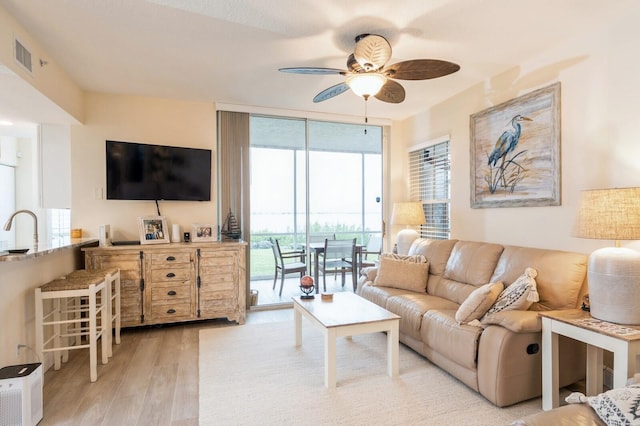 living room with ceiling fan, sink, and light wood-type flooring