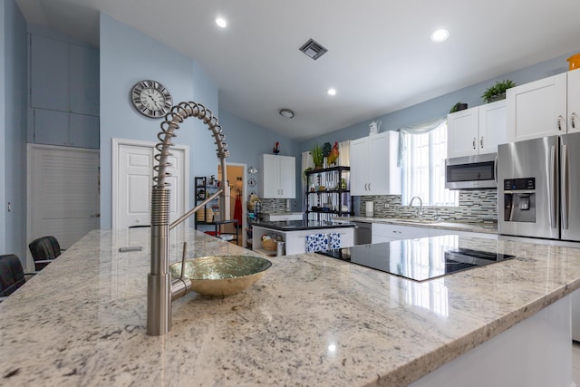 kitchen featuring a kitchen island, sink, white cabinets, stainless steel appliances, and light stone countertops