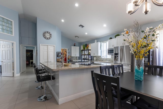 kitchen with white cabinetry, a center island, stainless steel appliances, light stone countertops, and decorative backsplash