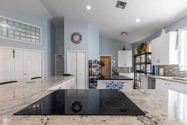 kitchen with sink, white cabinetry, black electric stovetop, light stone countertops, and vaulted ceiling