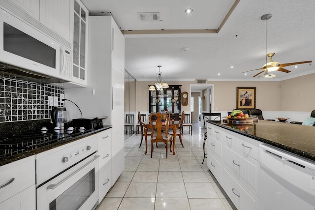 kitchen with light tile patterned floors, white appliances, dark stone countertops, white cabinets, and decorative light fixtures