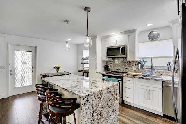 kitchen featuring a kitchen island, white cabinetry, sink, hanging light fixtures, and stainless steel appliances