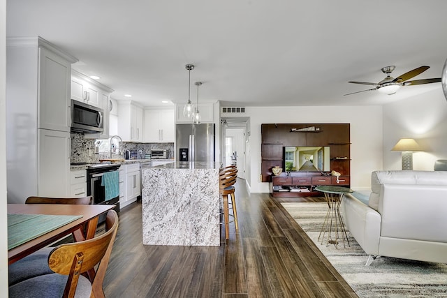 kitchen featuring a breakfast bar, appliances with stainless steel finishes, backsplash, hanging light fixtures, and a center island