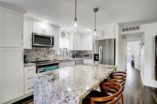 kitchen featuring a breakfast bar, white cabinets, hanging light fixtures, a center island, and stainless steel appliances