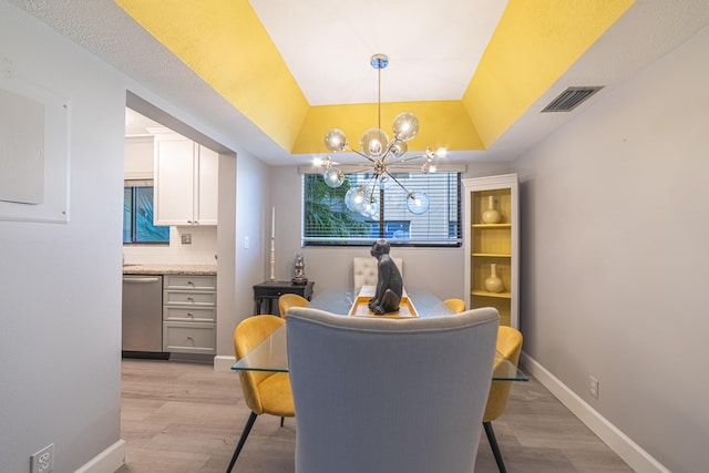 dining space with light hardwood / wood-style flooring, a notable chandelier, and a tray ceiling