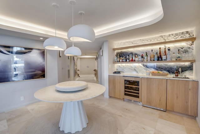 bar with light brown cabinetry, decorative light fixtures, tasteful backsplash, beverage cooler, and a raised ceiling