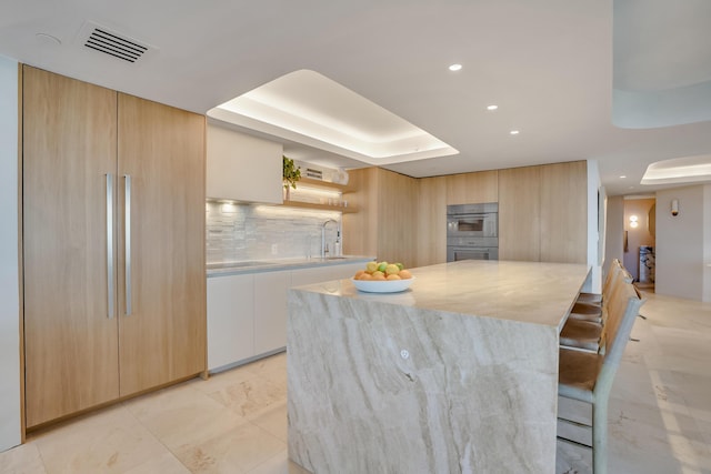 kitchen with light brown cabinetry, white cabinetry, tasteful backsplash, a raised ceiling, and a kitchen island