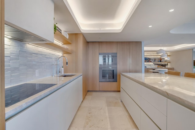 kitchen featuring double oven, white cabinetry, sink, a raised ceiling, and light stone countertops