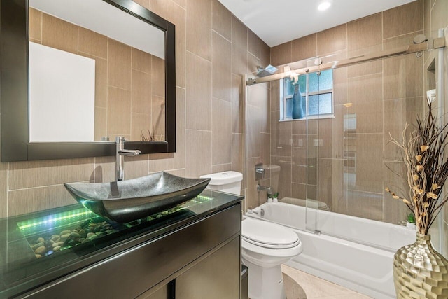 full bathroom featuring toilet, vanity, shower / bath combination with glass door, and tile walls