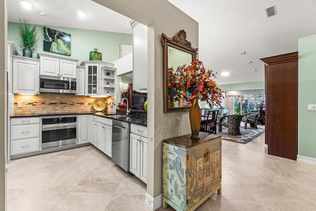 kitchen featuring sink, white cabinetry, dark stone counters, stainless steel appliances, and backsplash