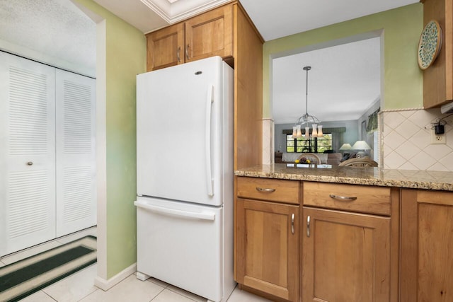 kitchen with an inviting chandelier, light tile patterned floors, white refrigerator, light stone countertops, and backsplash