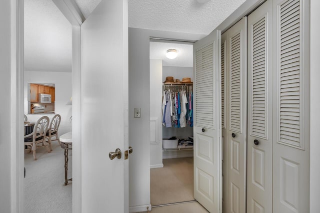 hallway with light colored carpet and a textured ceiling