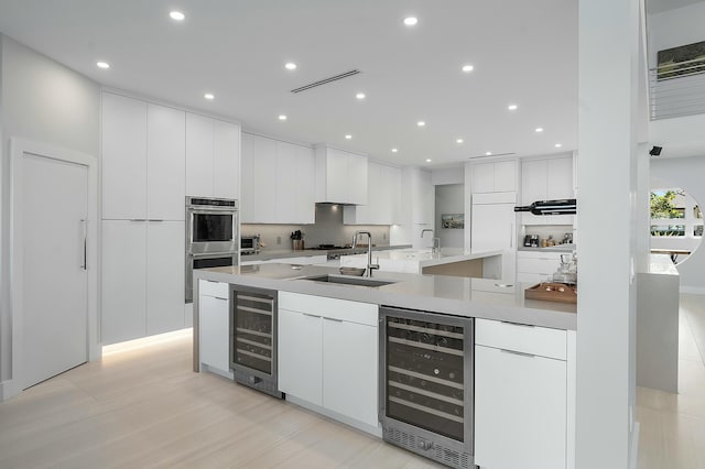 kitchen with wine cooler, white cabinetry, stainless steel double oven, and sink