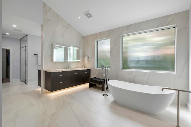 bathroom featuring vaulted ceiling, vanity, a bathtub, and tile walls