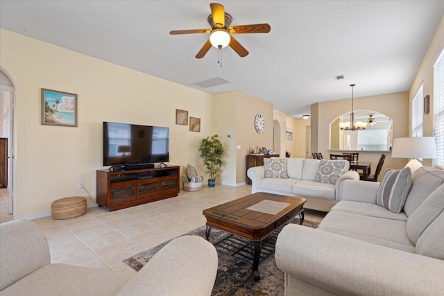 tiled living room with ceiling fan with notable chandelier